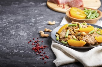 Fried pork with peaches, cashew and green beans on a black concrete background. side view, copy