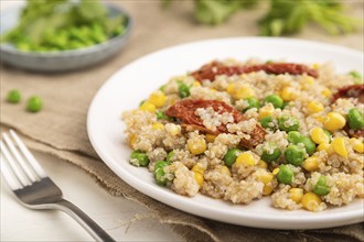 Quinoa porridge with green pea, corn and dried tomatoes on ceramic plate on a white wooden