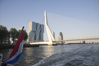 Dutch national flag flying at the back of a boat with buildings of De Rotterdam and Erasmusbrug in