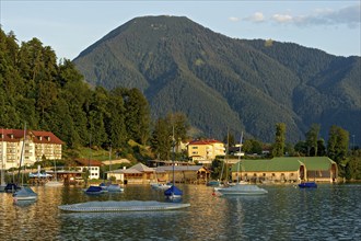 Tegernsee with sailing boats and boat huts, warm evening light, town Tegernsee, mountain Wallberg,