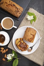 Homemade cake with raisins, almonds, soft caramel and a cup of coffee on a black concrete