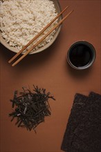 Leaves and chopped Nori shavings, with a cup of boiled rice, top view, on a brown background,