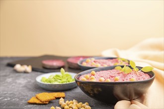 Hummus with beet and microgreen basil sprouts in ceramic bowl on a black concrete background and