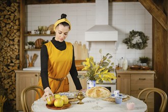 A woman in a yellow sleeveless sundress takes an apple from a tray standing in country style