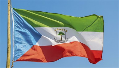 The flag of Equatorial Guinea flutters in the wind, isolated against a blue sky