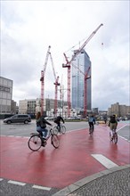 People on bicycles crossing a red carriageway, construction cranes in the background, Berlin,