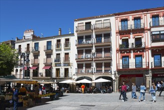 Urban square with people, buildings with balconies and shops under a clear blue sky, Plaza Mayor,