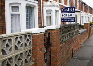 Estate agent for sale sign outside red brick terraced house in central Swindon, England, United