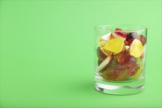 Various fruit jelly candies in drinking glass on green pastel background. side view, copy space