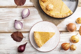 Autumn onion pie decorated with leaves and cup of coffee on white wooden background and linen