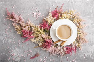 Pink and red astilbe flowers and a cup of coffee on a gray concrete background. Morninig, spring,