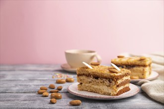 Honey cake with milk cream, caramel, almonds and a cup of coffee on a gray and pink background and