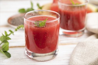 Watermelon juice with chia seeds and mint in glass on a white wooden background with linen textile.