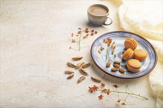 Orange macarons or macaroons cakes with cup of coffee on a white concrete background and linen