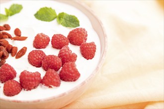 Yogurt with raspberry and goji berries in ceramic bowl on white concrete background and orange