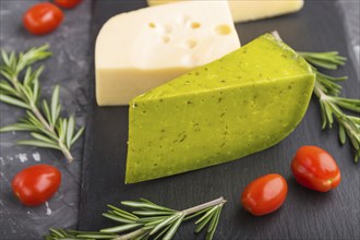 Green basil cheese and various types of cheese with rosemary and tomatoes on black slate board on a