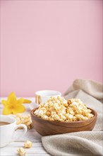 Popcorn with caramel in wooden bowl and a cup of coffee on a white and pink background and linen