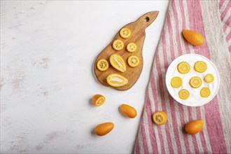 Greek yogurt with kumquat pieces in a white plate on a white wooden background, top view, flat lay,