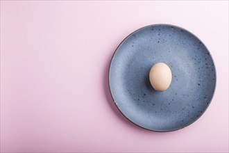 Raw uncooked single egg on a blue ceramic plate on a pink pastel background. top view, copy space