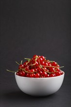 Fresh red currant in white bowl on black background. side view, copy space