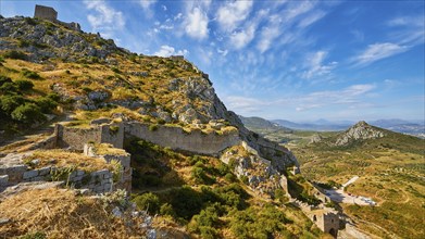 The ruins of an ancient castle on a hill overlooking a path and surrounding green land, Archaic