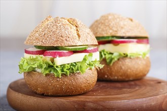 Sandwiches with cheese, radish, lettuce and cucumber on wooden board on a gray concrete background.