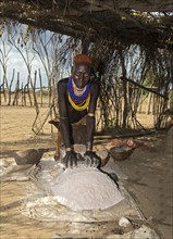 Woman from the Arbore ethnic group grinding red sorghum millet on a grinding stone, Southern Omo