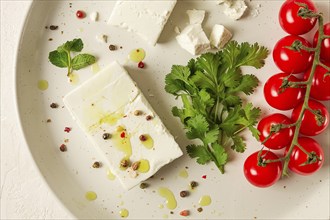 Feta cheese, for salads, with cherry, green butter, greens, on a white plate, appetizer, top view,