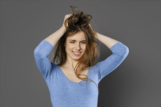 Young woman fooling around and mussing her hair with her hands over grey studio background