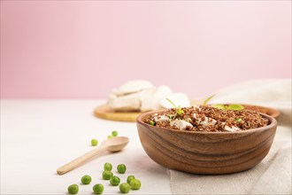 Quinoa porridge with green pea and chicken in wooden bowl on a white and pink background and linen