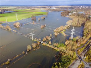 An aerial photograph shows flooded fields and landscape with electricity pylons and cloudy sky,