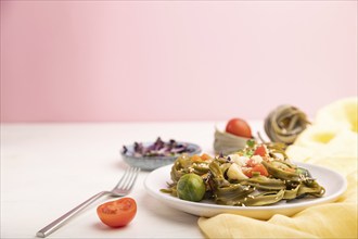 Tagliatelle green spinach pasta with tomato, pea and microgreen sprouts on a white and pink