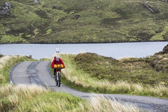 Lonely female biker cycling through the Scottish Highlands on heavily laden touring bicycle along