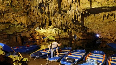 Man preparing boats in an illuminated cave with stalactites, stalactite cave, Diros Cave, Glyafada