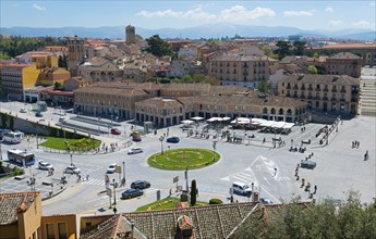 Lively town square with surrounding historic buildings and a green circular flower bed, Segovia,