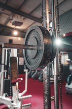 Dumbbell bar with weights on a machine in a fitness studio. In the background red floor, historic