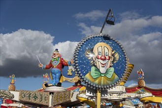 Colourfully decorated carousel with clown figure and blue sky in the background at a fairground,