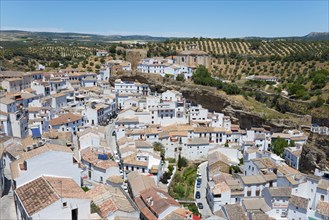 A white village with tiled roofs, embedded in a rock formation, surrounded by rural landscape, cave