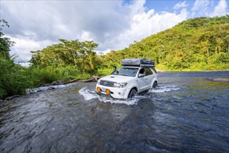 Toyota off-road vehicle with roof tent drives through a wide river in the rainforest, Alajuela