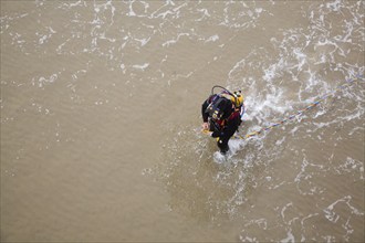 Looking down from above at professional diver on a beach about to enter the sea to work on the pier