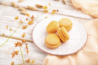 Orange macarons or macaroons cakes with cup of apricot juice on a white wooden background and