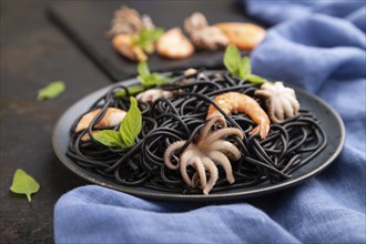 Black cuttlefish ink pasta with shrimps or prawns and small octopuses on black concrete background