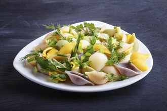 Conchiglie colored pasta with fresh greengrocery on black wooden background. close up, selective