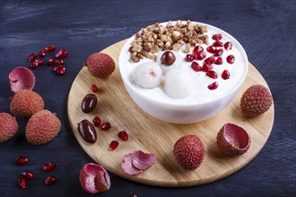 Greek yogurt with lychee, pomegranate seeds and granola in a white plate on a black wooden