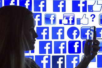 Silhouette of a woman with a smartphone in her hand in front of a Facebook logo, 12/01/2016