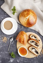 Homemade yeast buns and rolls with poppy seeds and honey on a black concrete background with a cup