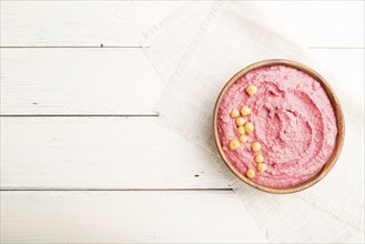 Hummus with beet in wooden bowl on a white wooden background and linen textile. Top view, flat lay,