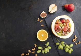 Vegetarian fruit salad of watermelon, grapes, figs, pear, orange, cashew on slate board on a black