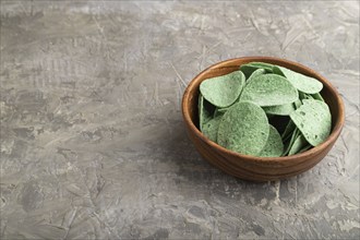 Green potato chips with herbs in wooden bowl on gray concrete background. Side view, copy space