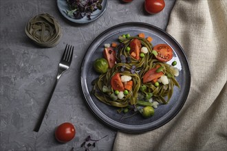 Tagliatelle green spinach pasta with tomato, pea and microgreen sprouts on a gray concrete